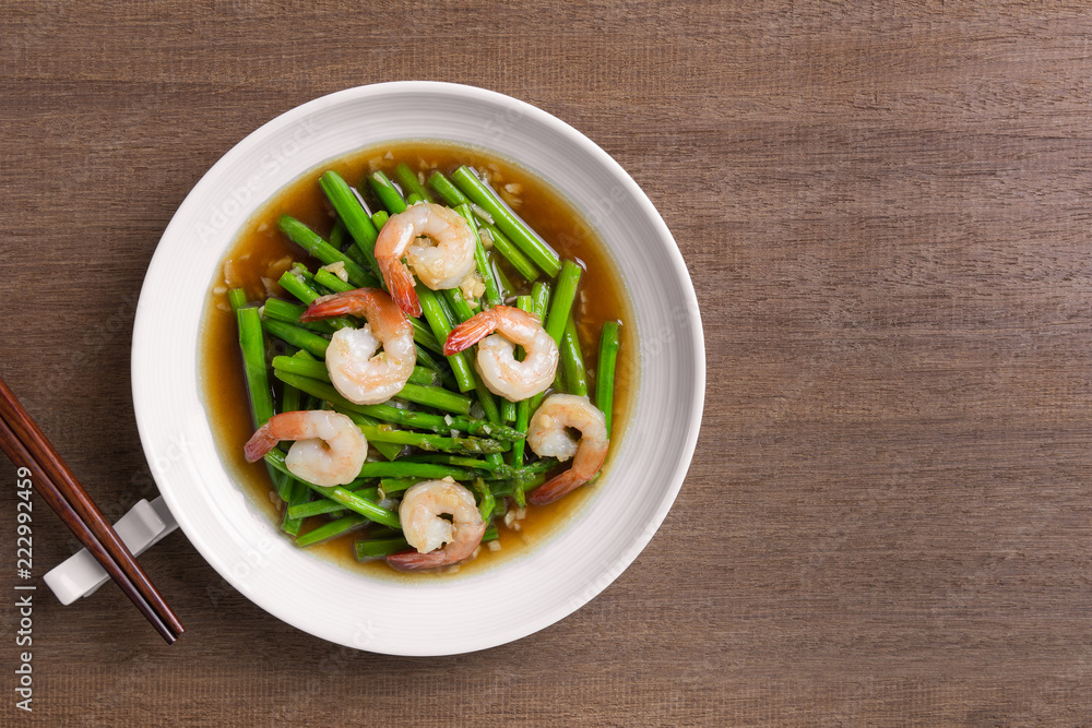 top view of stir fried asparagus and shrimp with oyster sauce in a ceramic dish on wooden table. asian homemade style food concept. top view of stir fried asparagus and shrimp with oyster sauce in a ceramic dish on wooden table. asian homemade style food concept.