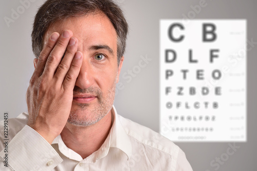 Middle-aged man covering an eye for optical revision letter chart photo