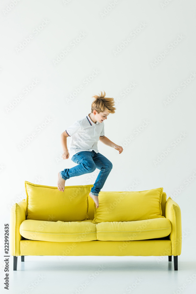 adorable boy in casual clothes jumping on yellow sofa on white adorable boy in casual clothes jumping on yellow sofa on white
