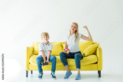 happy mother showing yes gesture after winning video game on yellow sofa on white