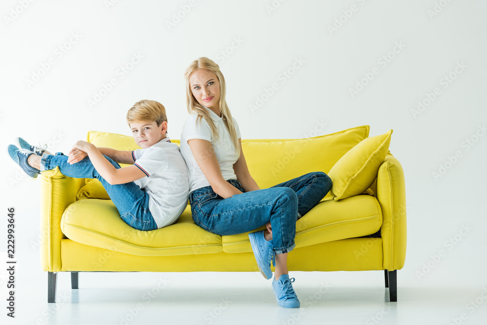 mother and son sitting back to back on yellow sofa on white mother and son sitting back to back on yellow sofa on white