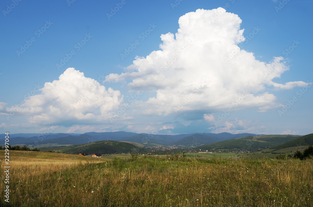 Big cumulus clouds in the blue sky over Transylvania in the evening after rain, Romania; Picturesque rural landscape
