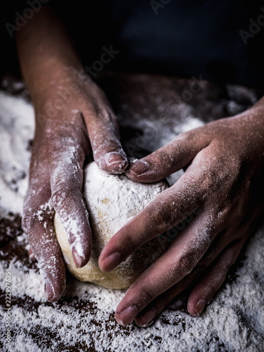 pastry chef hand kneading Raw Dough with sprinkling white flour over kitchen table.