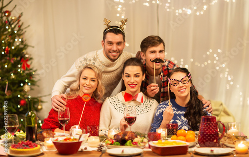 holidays and celebration concept - happy friends with party props having christmas dinner at home