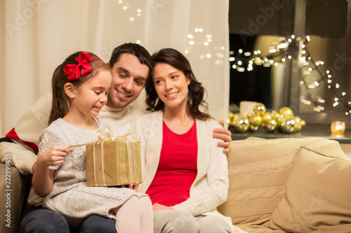 holidays, family and celebration concept - happy mother, father and little daughter with christmas present at home