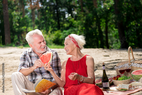 Fresh watermelon. Positive emotional couple of pensioners smiling and eating watermelon while having a picnic