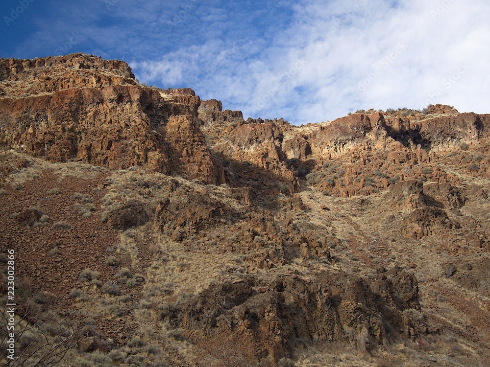 Rough and jagged cliff on a sfeep hill with green spring wild grasses and a beautiful blue sky in Central Oregon. Rough and jagged cliff on a sfeep hill with green spring wild grasses and a beautiful blue sky in Central Oregon.