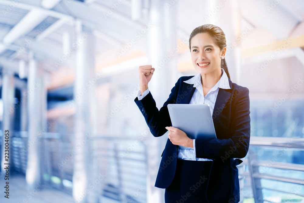 Business woman wearing a blue suit, Asian standing holding a laptop with a confident smile. Standing with the admiration of accomplished work, the goal is to make money earning bitcoins. copy space Business woman wearing a blue suit, Asian standing holding a laptop with a confident smile. Standing with the admiration of accomplished work, the goal is to make money earning bitcoins. copy space