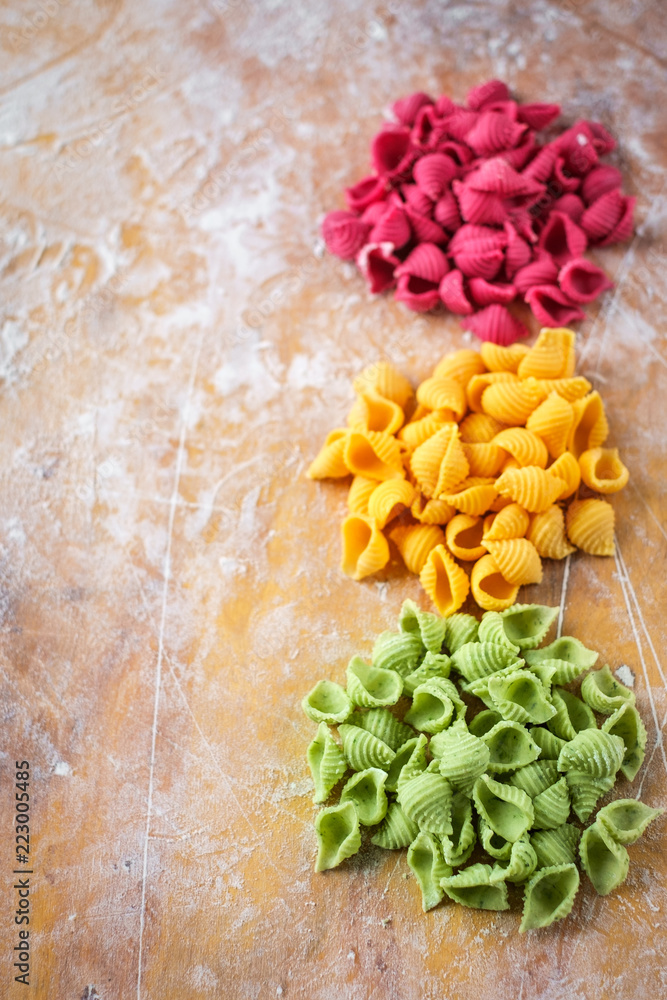 raw colored pasta on the kitchen wooden table with flour, top view