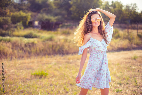 beautiful young woman in dress and sunglasses having fun with hair outdoor in countryside on a warm summer day
