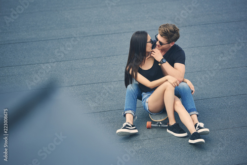 beautiful multiethnic couple hugging and sitting on skateboard