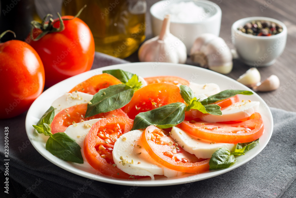 Photo of Caprese Salad with tomatoes, basil, mozzarella, olives and olive oil on wooden background. Italian traditional caprese salad ingredients. Mediterranean, organic and natural food concept. Photo of Caprese Salad with tomatoes, basil, mozzarella, olives and olive oil on wooden background. Italian traditional caprese salad ingredients. Mediterranean, organic and natural food concept.