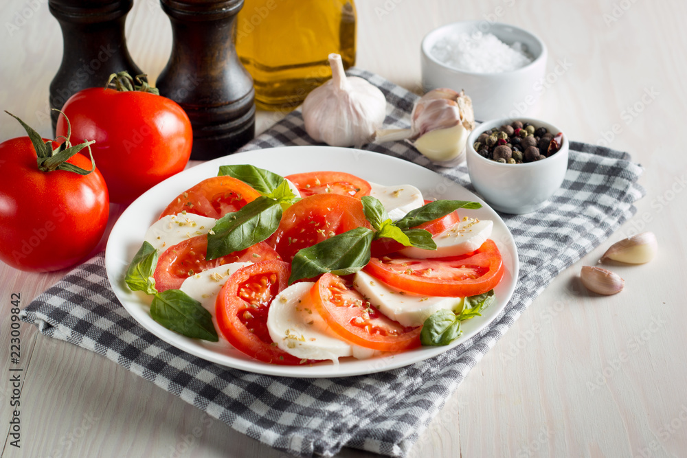 Photo of Caprese Salad with tomatoes, basil, mozzarella, olives and olive oil on wooden background. Italian traditional caprese salad ingredients. Mediterranean, organic and natural food concept. Photo of Caprese Salad with tomatoes, basil, mozzarella, olives and olive oil on wooden background. Italian traditional caprese salad ingredients. Mediterranean, organic and natural food concept.