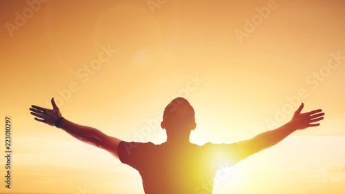 Young man standing outstretched at sunset. Bright solar glow and sky