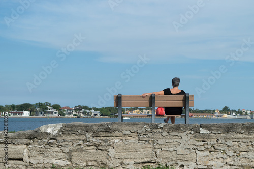 Unidentifiable old woman sitting on a bench, looking at the river and horizon, thinking about her life 