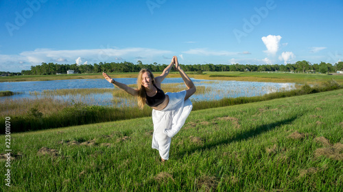 blonde woman spiritual doing yoga king dance standing pulling bow Natarajasana / Dandayamana Dhanurasana pose in nature