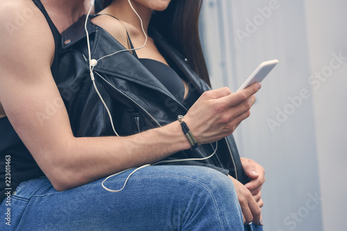 cropped view of stylish couple listening music with earphones and using smartphone