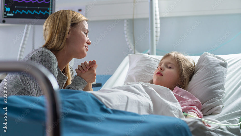 Cute Little Girl Sleeps on the Bed in the Children's Hospital, Her Mother Sits Beside, Worrying but Hopeful. Modern Pediatric Ward. Cute Little Girl Sleeps on the Bed in the Children's Hospital, Her Mother Sits Beside, Worrying but Hopeful. Modern Pediatric Ward.