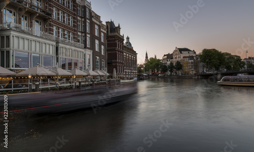 Amsterdam canal at dusk. A wide canal  with a moving canal boat sailing past the houses