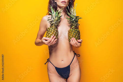 Obraz na plátně Anonymous young female in black panties holding ripe pineapples near boobies whi
