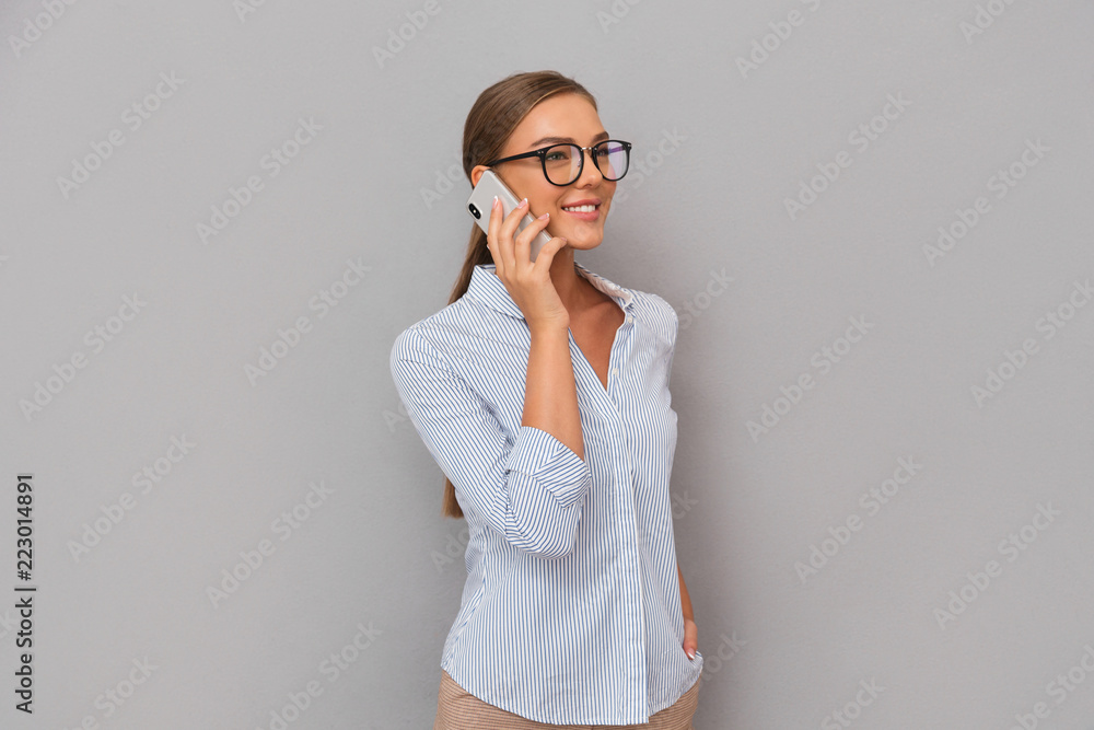 Happy business woman standing over grey wall background talking by mobile phone. Happy business woman standing over grey wall background talking by mobile phone.