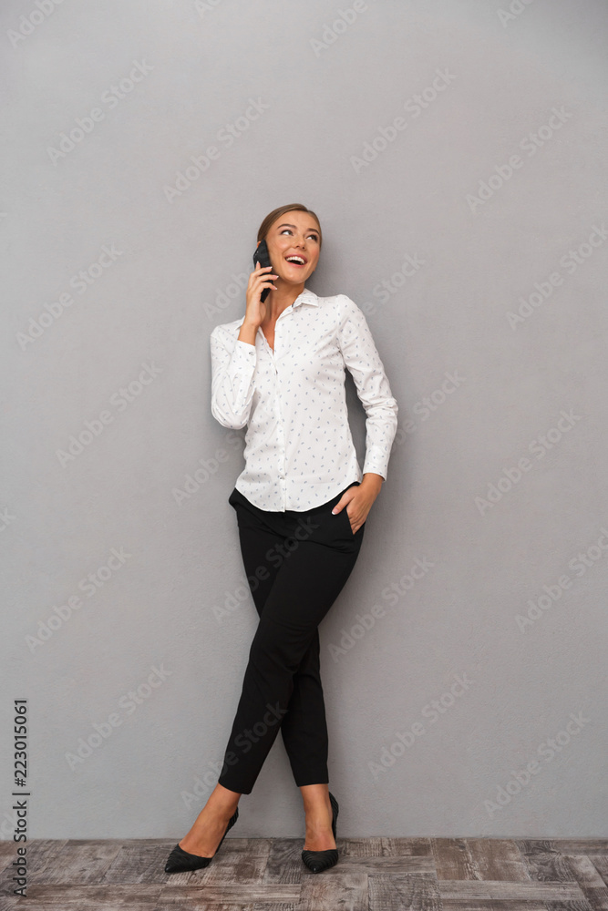 Happy business woman standing over grey wall background talking by mobile phone. Happy business woman standing over grey wall background talking by mobile phone.