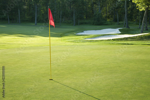 Golf green with red flag in late afternoon sunlight