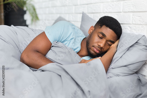 Fotografie Young african-american man sleeping in bed at home