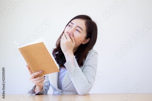 Asian business women in white suit holding and looking at a notebook while she yawning on white background.