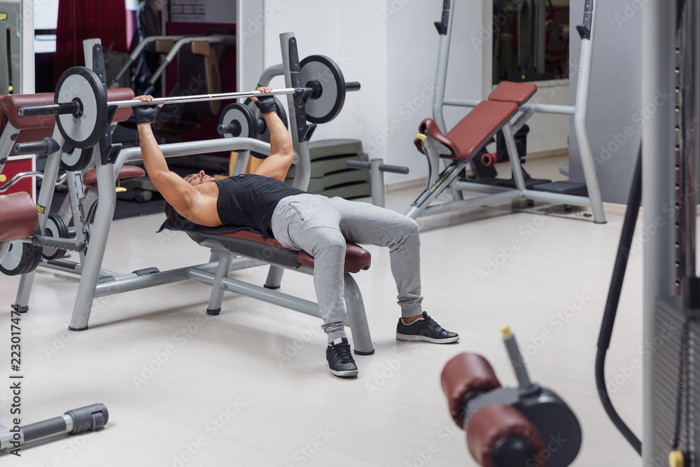 Weightlifter or bodybuilder lying on a bench lifting a barbell weight in a gym during training in a healthy active lifestyle and fitness concept Weightlifter or bodybuilder lying on a bench lifting a barbell weight in a gym during training in a healthy active lifestyle and fitness concept