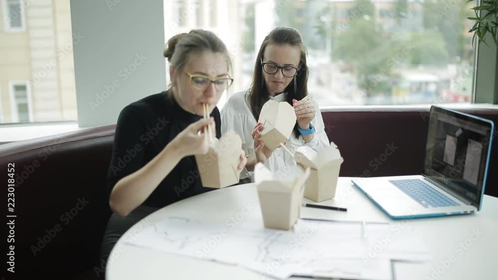 Two hungry businesswoman decide to eat not looking up from his work. Business lunch while working in the office Two hungry businesswoman decide to eat not looking up from his work. Business lunch while working in the office