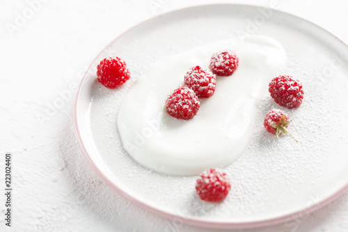 plate with homemade yogurt and ripe raspberries with on white table