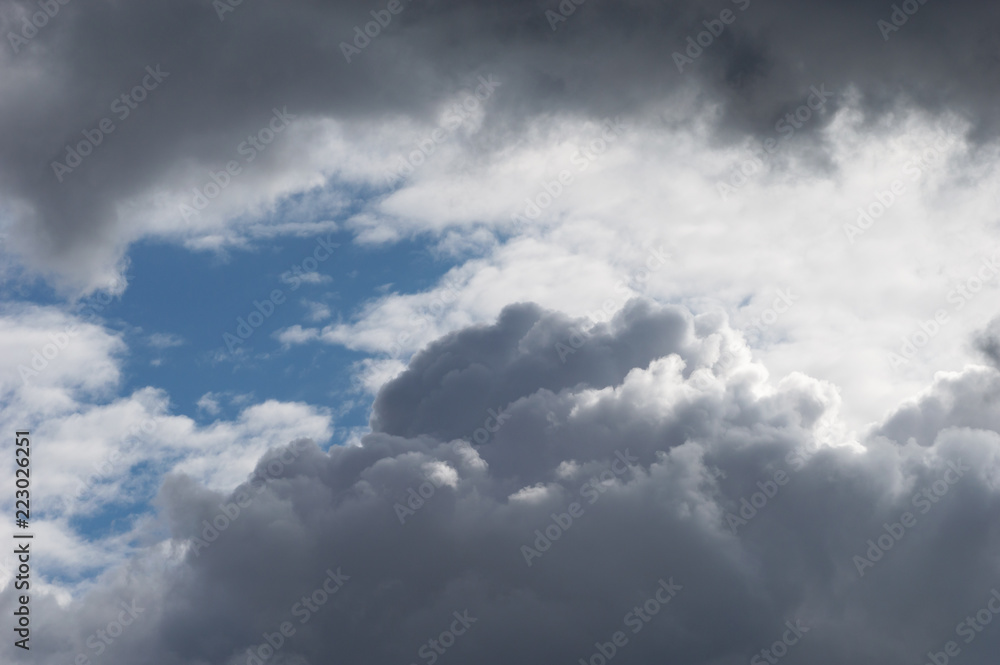 Billowing clouds with blue sky. Moody stormy weather with both grey clouds and contrasting brightly lit white clouds.