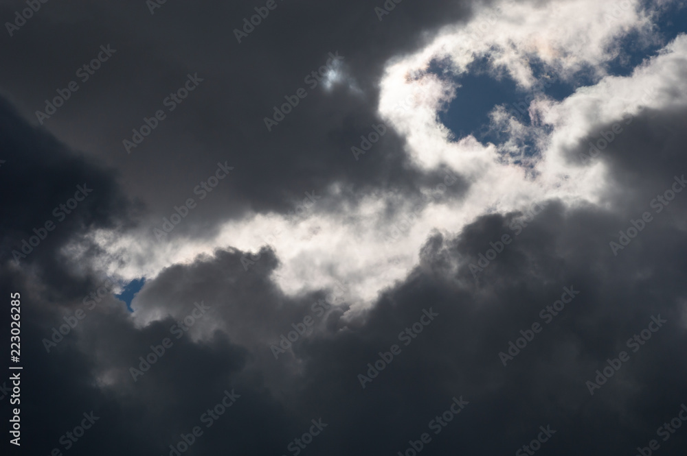 Stormy ominous clouds with blue sky. Moody oppressive weather with both dark grey clouds and contrasting brightly lit white clouds.