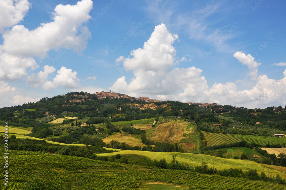 Obraz premium Distant town on top of a hill during a beautiful sunny day over big green fields.