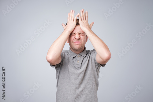 Canvas Print Young caucasian man holding hands on head and closing his eyes