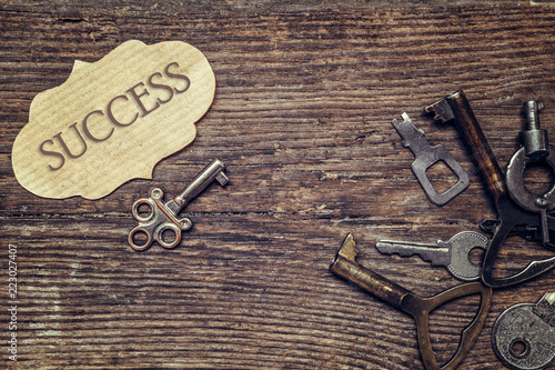 Old antique key and a set of vintage keys and an inscription success on a plate on a wooden background a flat top view, a concept of choosing success and achievements photo