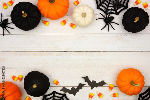 Halloween double border with black, orange and white decor and candy over a white wood background. Top view with copy space. photo