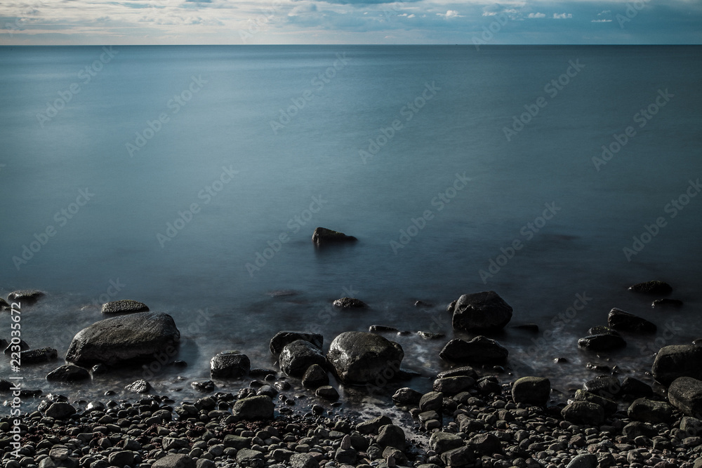 Obraz premium Standing at the shore where the ocean meets the land. It's the baltic sea in winter. A quiet, smooth evening in the middle of blue and grey light an colour.