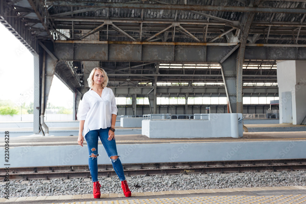 young beautiful girl in a white shirt, blue jeans and red shoes goes on the  platform at the old railway station Stock Photo | Adobe Stock