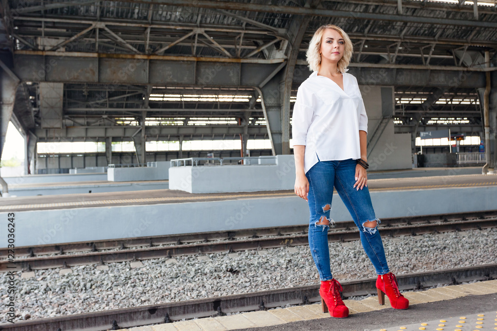 young beautiful in a white shirt, blue jeans and red shoes on platform at the old railway station Stock Photo | Adobe Stock