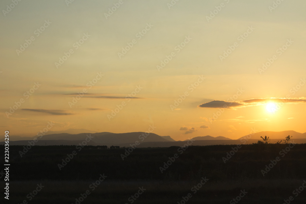 sunset on a field with mountains in backround