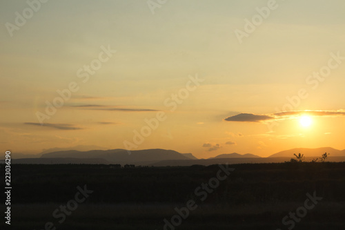 sunset on a field with mountains in backround