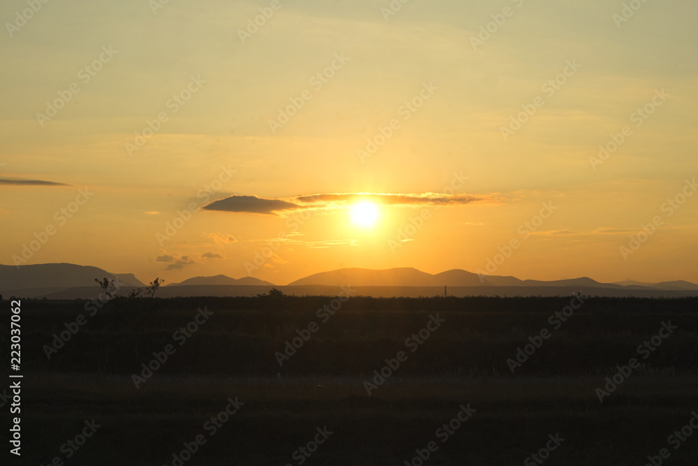 sunset on a field with mountains in backround