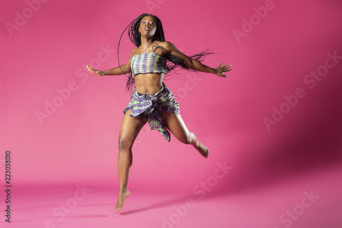 Obraz na płótnie Beautiful African Black girl wearing traditional colorful African outfit does a dramatic dance move against a colorful pink background w salonie