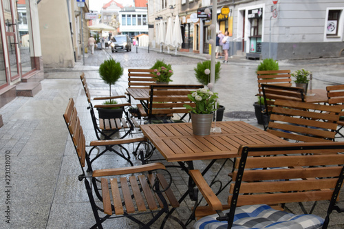 A metal bench with a round table and an empty chair in front of a cafe on the street