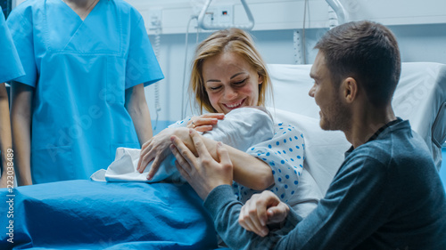 In the Hospital Mother Hold Newborn Baby, Supportive Father Lovingly Hugging Baby and Wife. Happy Family in the Modern Delivery Ward.