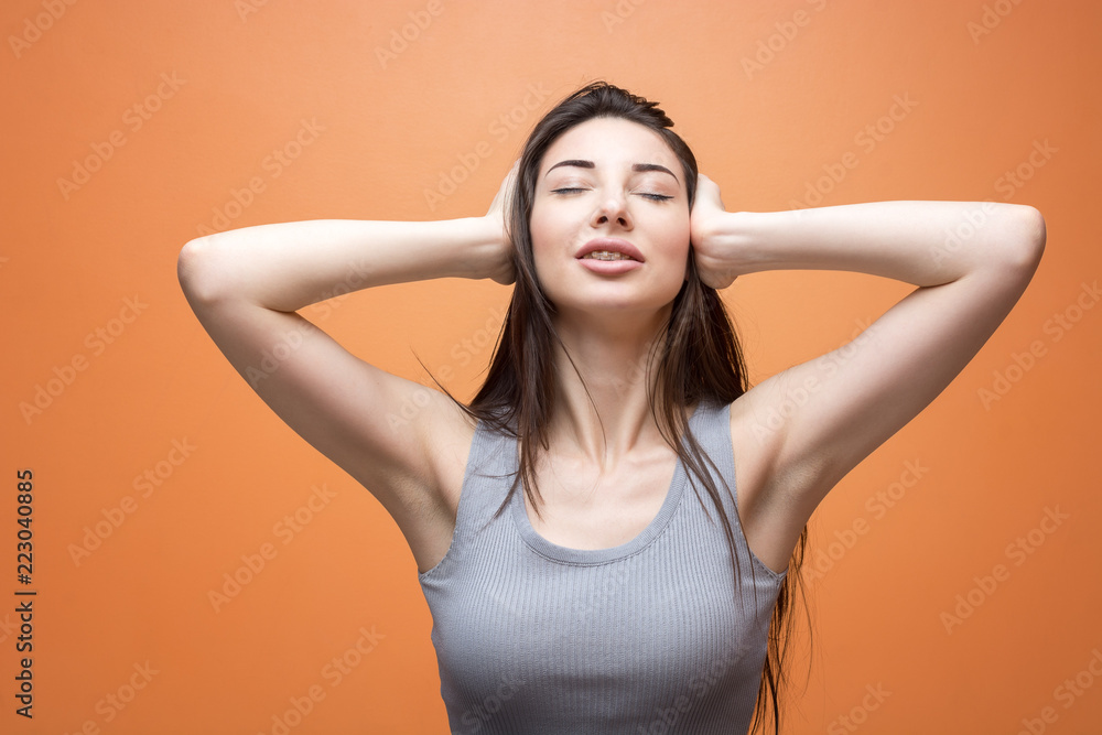 Closeup portrait of a young brunette girl in grey neutral shirt with her eyes closed, covering her ears, open mouth with braces Closeup portrait of a young brunette girl in grey neutral shirt with her eyes closed, covering her ears, open mouth with braces