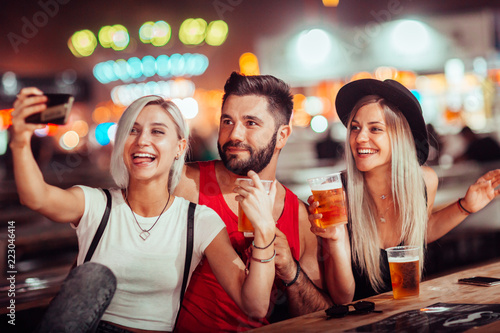 Group of friends drinking beer and taking selfie at music festival 
