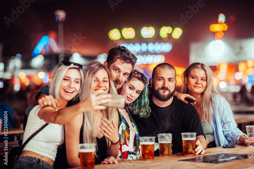 Group of friends drinking beer and taking selfie at music festival 